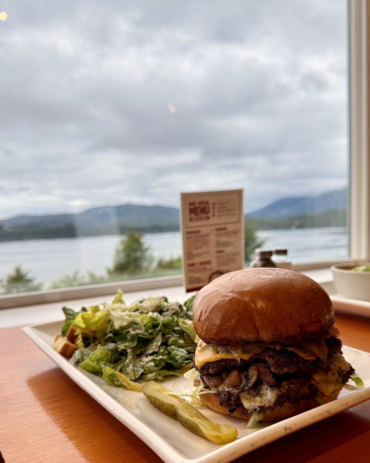 A mushroom Swiss double smash burger and Caesar salad on a window seat overlooking Prince Rupert harbour at OV Burger Bar