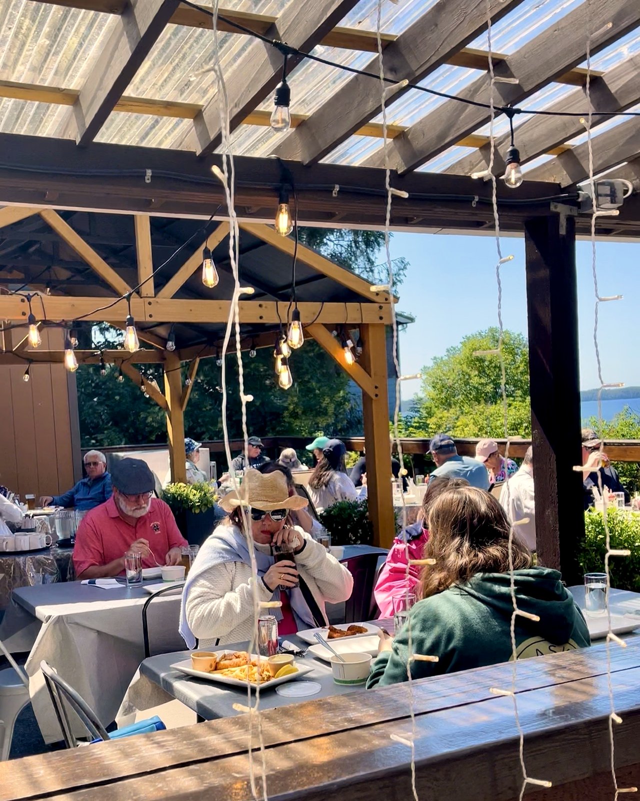 Guests dining under string lights on the OV outdoor patio, harbour view in the background, on a summer afternoon in Prince Rupert, BC