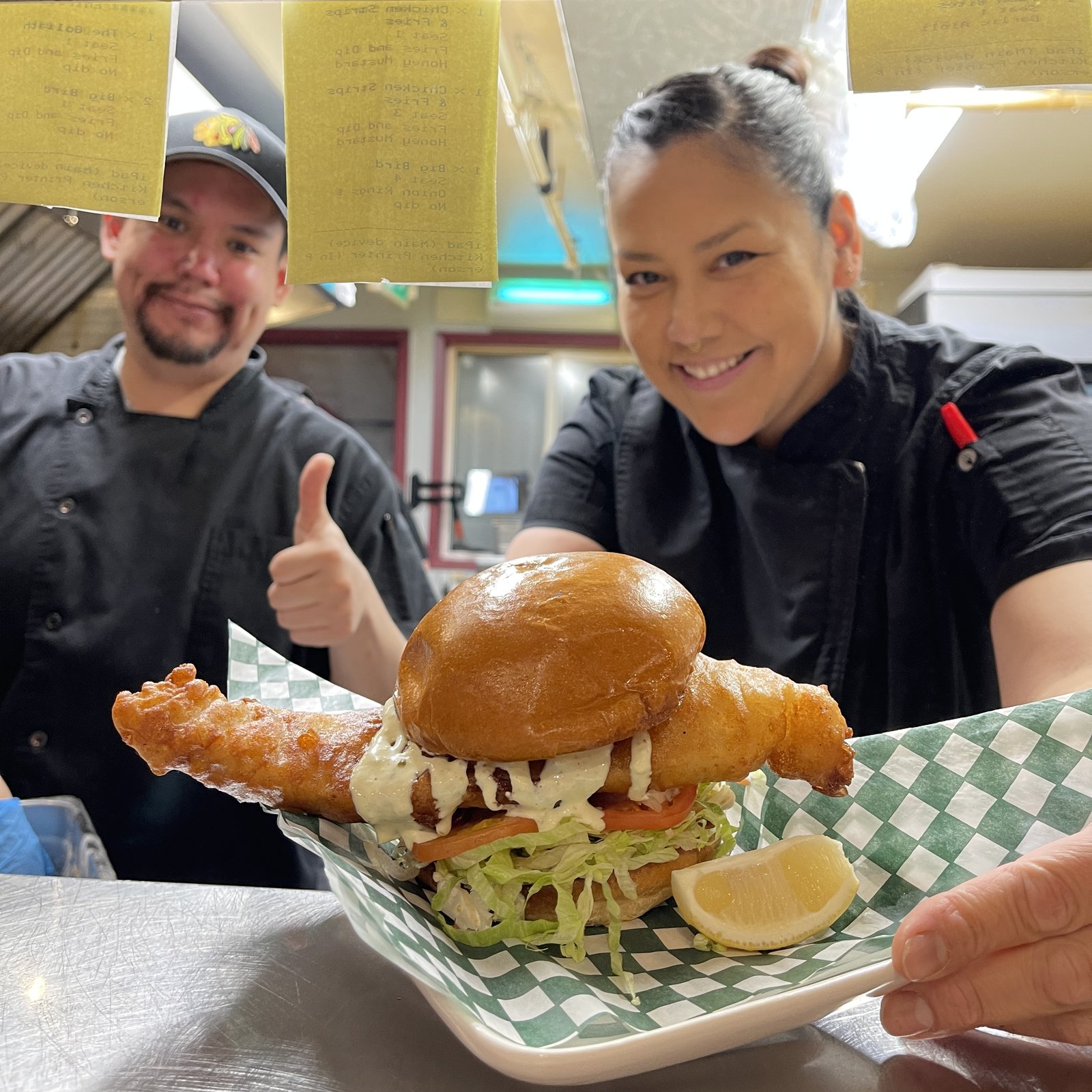OV Burger Bar kitchen staff holding up the Holy Ship fish burger in the kitchen