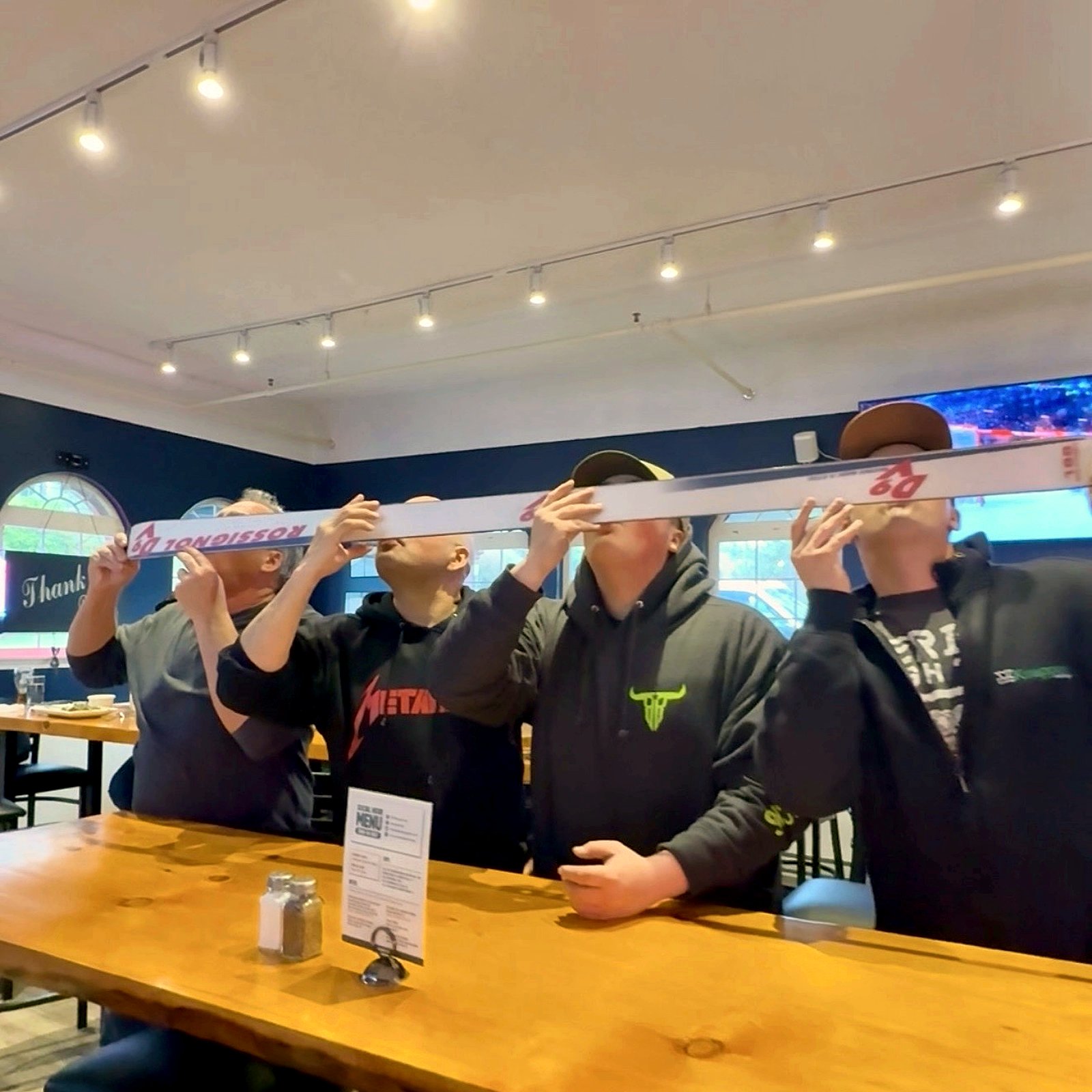 Four guests taking a group shot off the Shot Ski together at the bar inside OV Burger Bar, in the historic Ocean View Hotel in Prince Rupert, BC